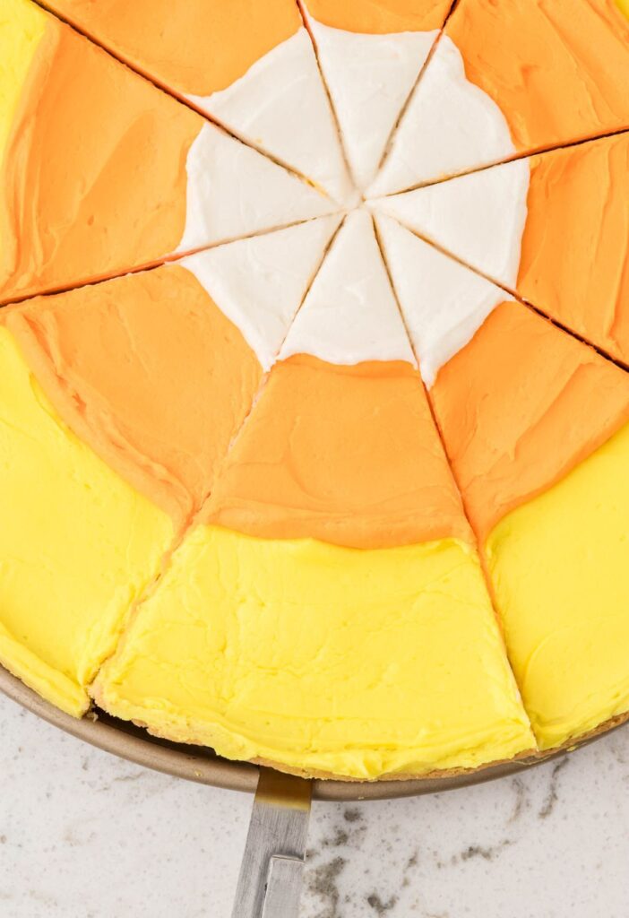 A dessert pizza with candy corn colors cut into slices.