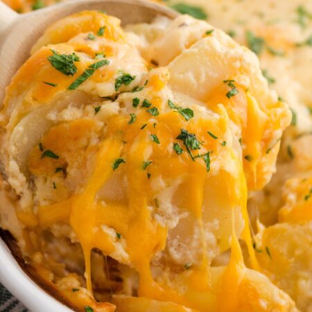 A white casserole dish with a serving spoon scooping some potatoes out of it.