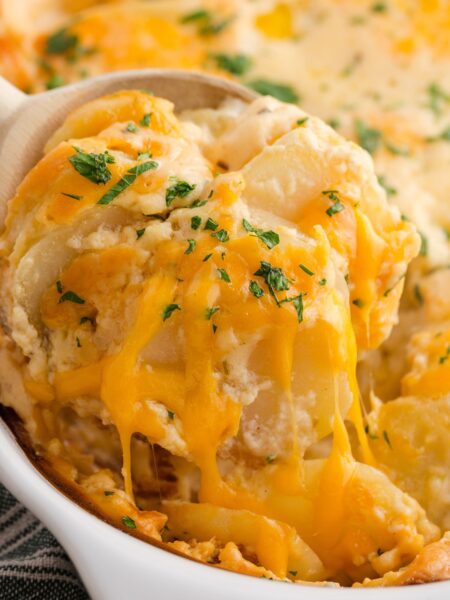 A white casserole dish with a serving spoon scooping some potatoes out of it.