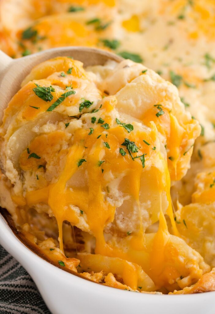 A white casserole dish with a serving spoon scooping some potatoes out of it. 