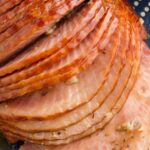 Sliced spiral cut ham with seasonings on the slices and garlic.