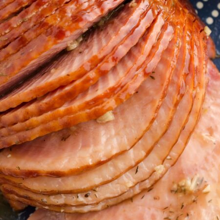 Sliced spiral cut ham with seasonings on the slices and garlic.