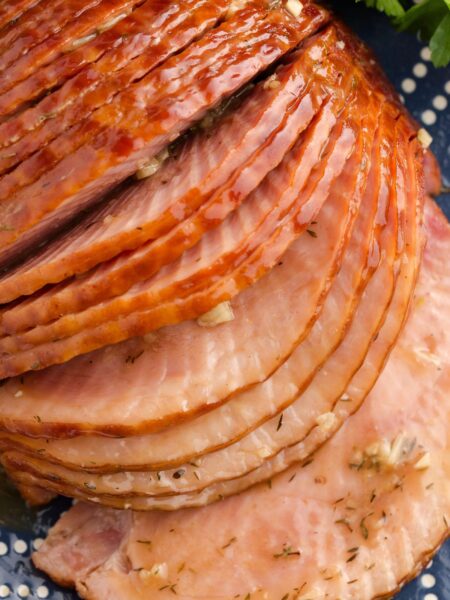 Sliced spiral cut ham with seasonings on the slices and garlic.