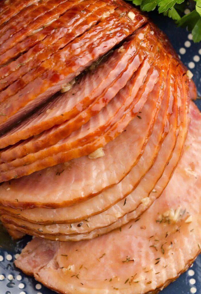 Sliced spiral cut ham with seasonings on the slices and garlic. 