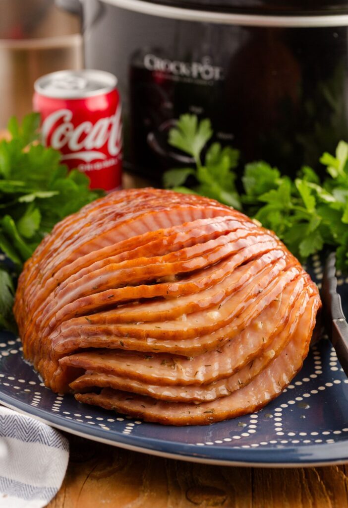 A blue plate with spiral sliced ham on it and a can of coke soda in the back. 
