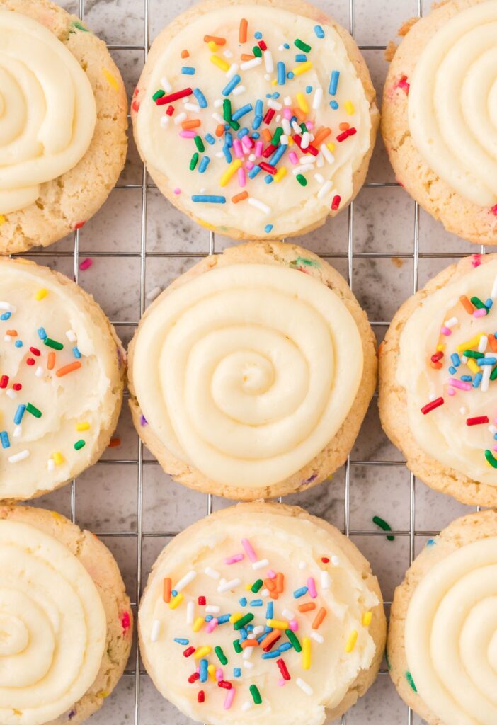 Top view of the cooling rack of funfetti cookies with some plain with frosting and others have sprinkles on the frosting. 