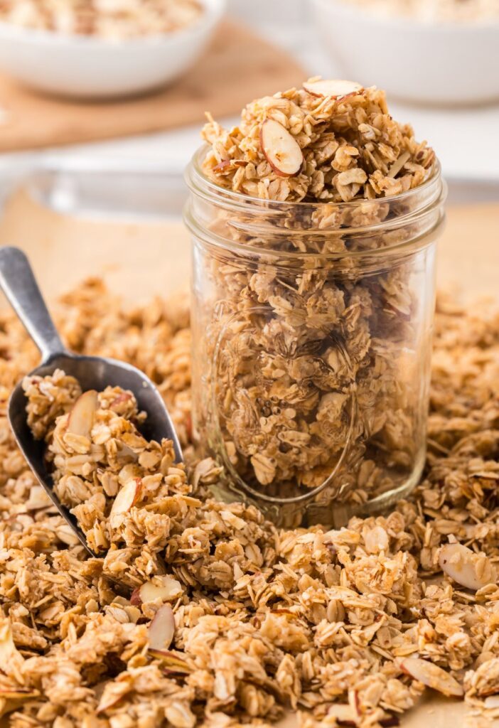 A tray of homemade granola with a scoop and a jar of it. 