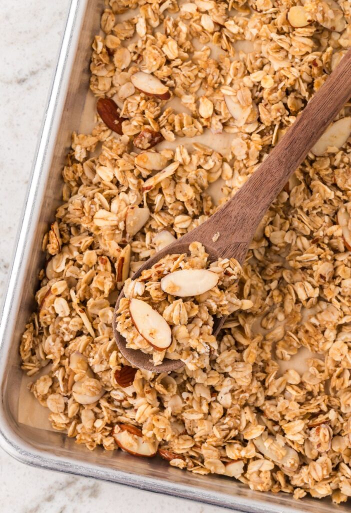A baking tray of cooked granola with a wooden spoon. 