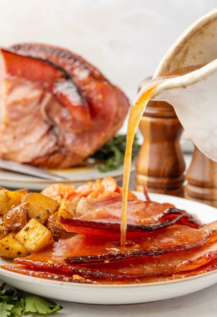 Gravy being poured over some slices of the oven baked honey glazed ham. 