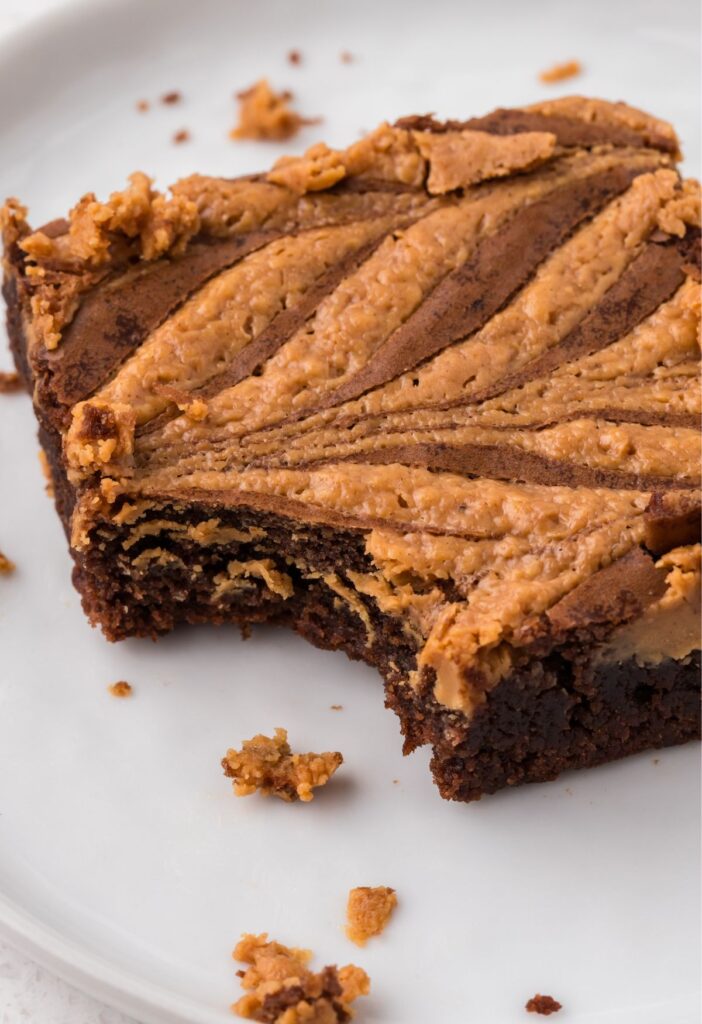 One brownie square on a white plate with crumbs and a bite taken out of the corner. 