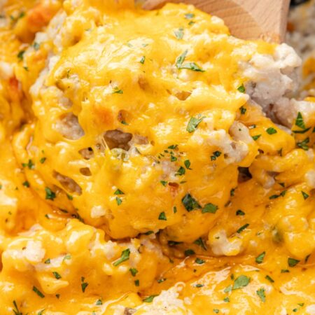 A slow cooker with the cheesy chicken and rice and a wooden serving spoon with some on it.