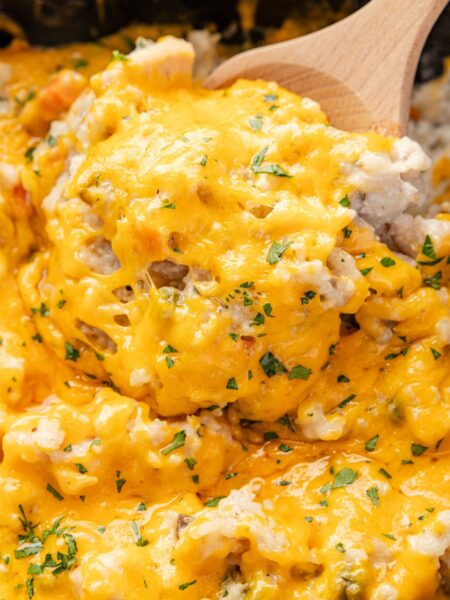 A slow cooker with the cheesy chicken and rice and a wooden serving spoon with some on it.