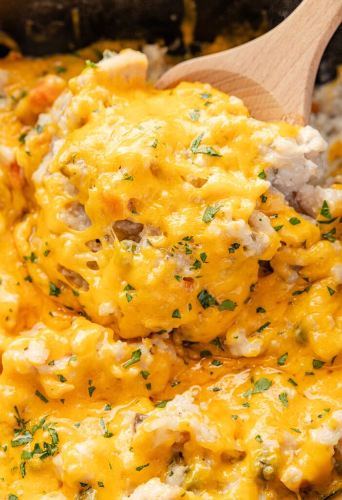 A slow cooker with the cheesy chicken and rice and a wooden serving spoon with some on it. 