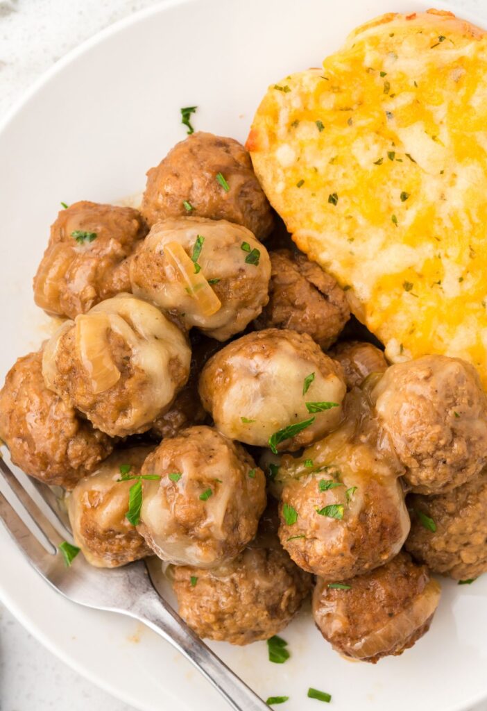 Serving of the meatballs with French onion soup on a plate with a piece of texas toast. 