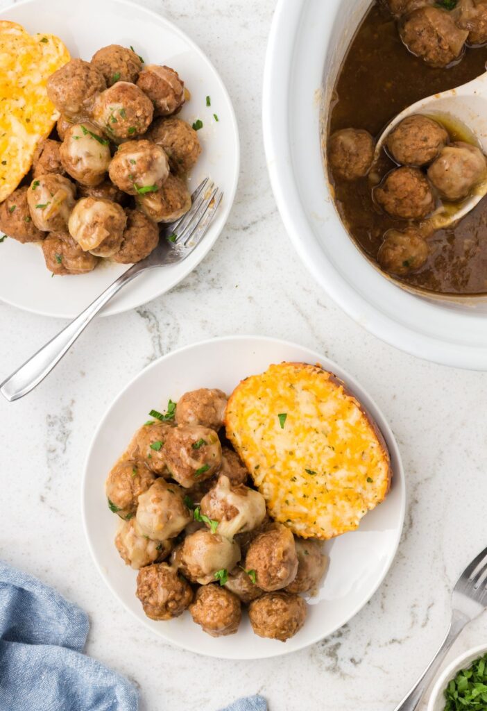 Top view of the slow cooker with a serving plate of the French onion meatballs. 