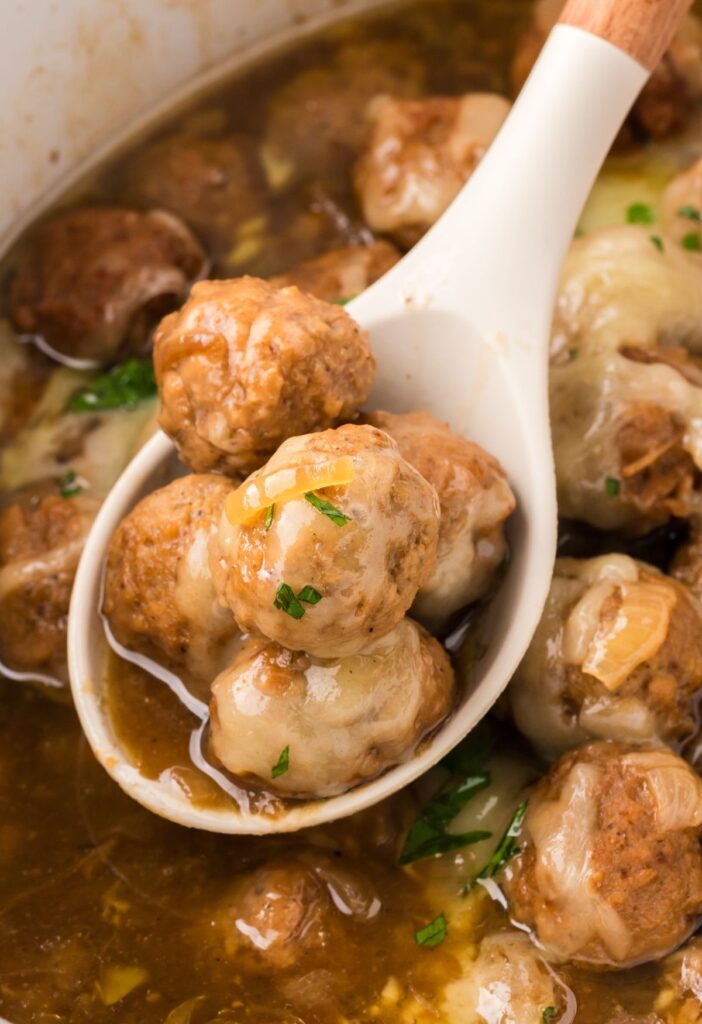 A serving spoon with meatballs on it above the slow cooker of meatballs and sauce. 