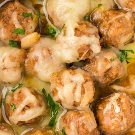 Close up of the meatballs with sauce and shredded gruyere cheese on top
