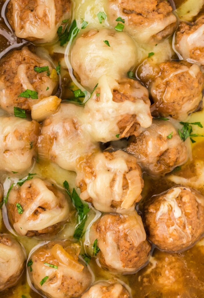Close up of the meatballs with sauce and shredded gruyere cheese on top