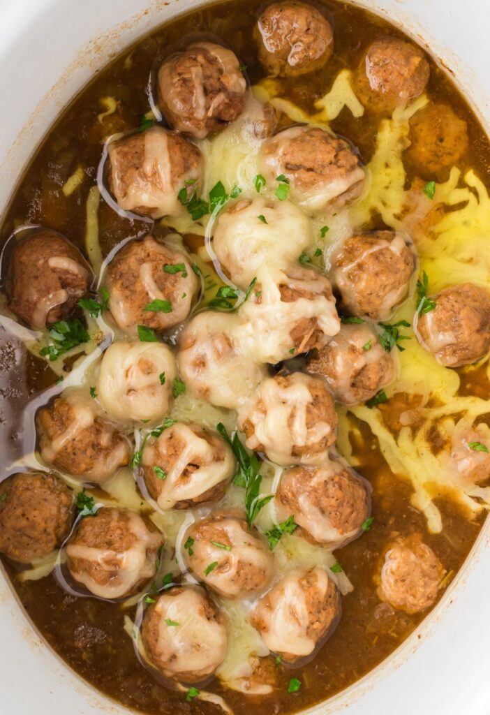 Top view of inside of a slow cooker with meatballs and cheese. 
