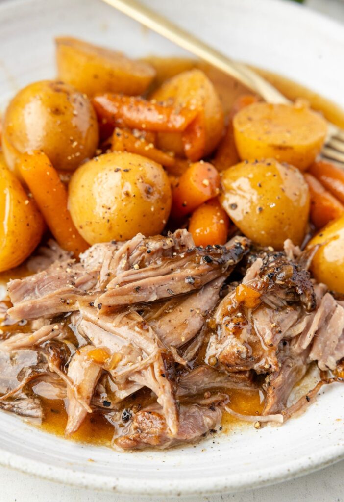 Hero shot of the cooked pork roast, shredded, on a plate with potatoes and carrots. 