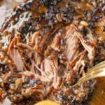 A pork roast cooked inside the slow cooker with a fork shredding it.