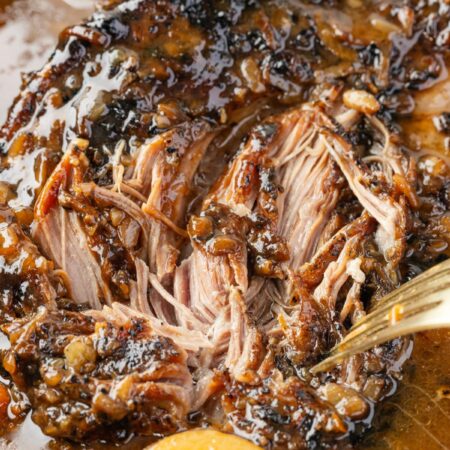 A pork roast cooked inside the slow cooker with a fork shredding it.