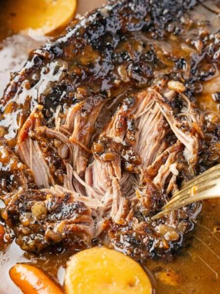 A pork roast cooked inside the slow cooker with a fork shredding it.