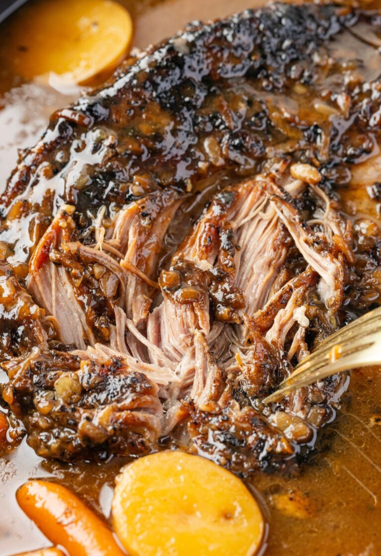 A pork roast cooked inside the slow cooker with a fork shredding it.