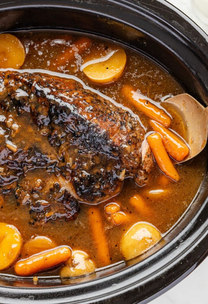 Pork roast inside the slow cooker with a spoon