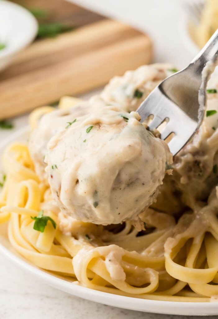 Plate of pasta with meatballs with one meatball on a fork. 