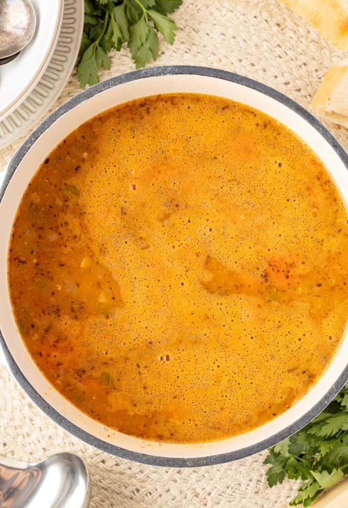 Soup pot with soup in it and parsley around it. 