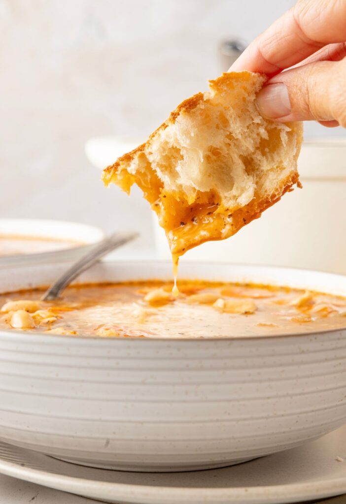 A piece of bread being dipped into a bowl of soup