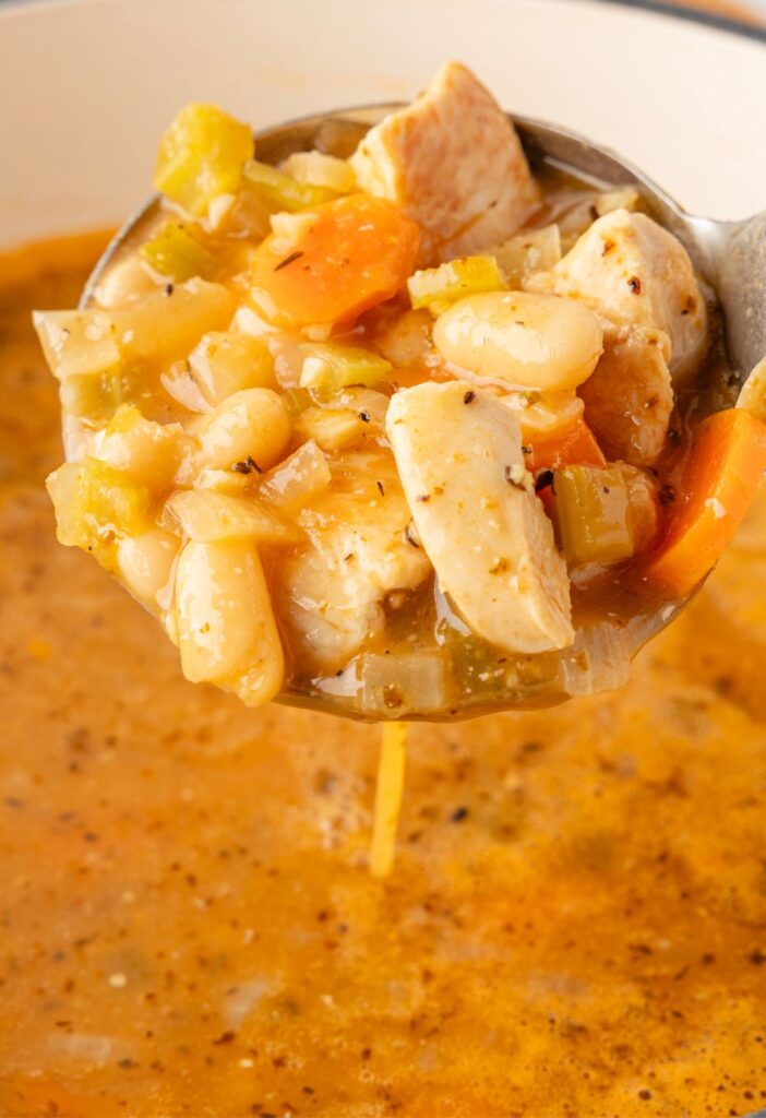 A scoop of the soup inside the soup ladle above the pot of soup. 