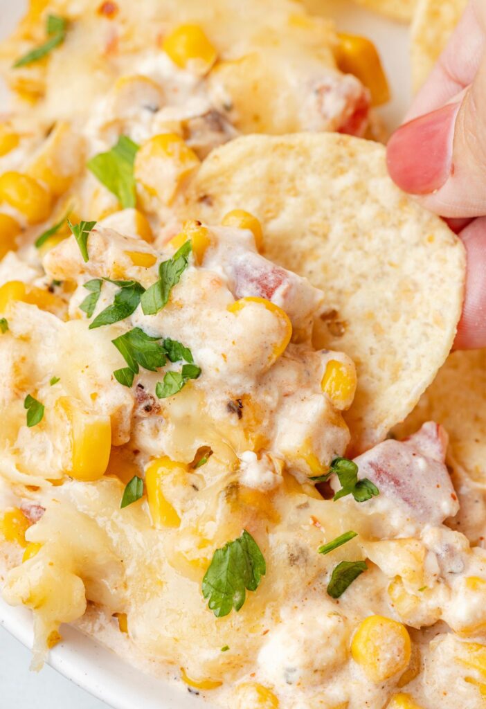 A serving of the corn dip with a hand holding a chip dipped into it.