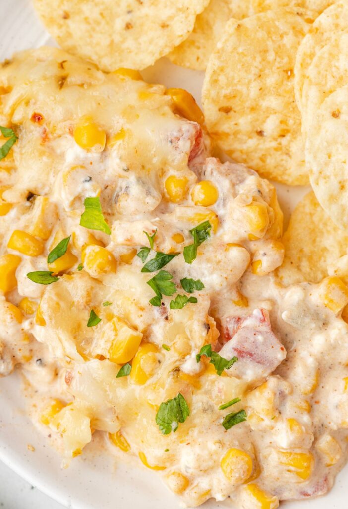 Serving of the hot corn dip on a white plate with tortilla chips.