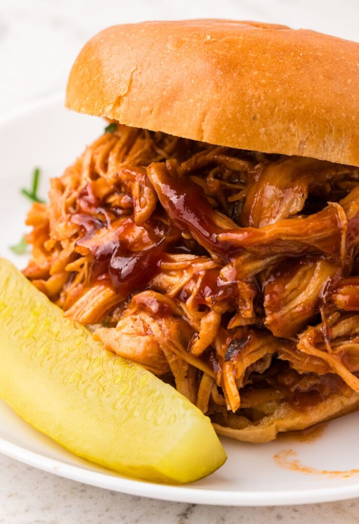 A sandwich with shredded bbq chicken on it and a pickle. 