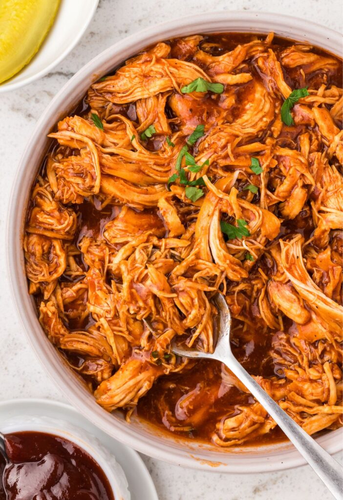 Shredded bbq chicken in a bowl with a serving spoon. 