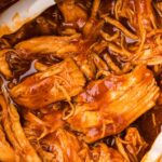 Close up of the shredded saucy bbq chicken inside the instant pot with tongs.