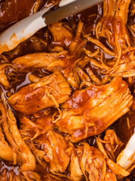 Close up of the shredded saucy bbq chicken inside the instant pot with tongs.