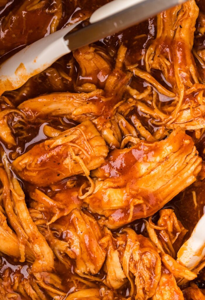Close up of the shredded saucy bbq chicken inside the instant pot with tongs. 