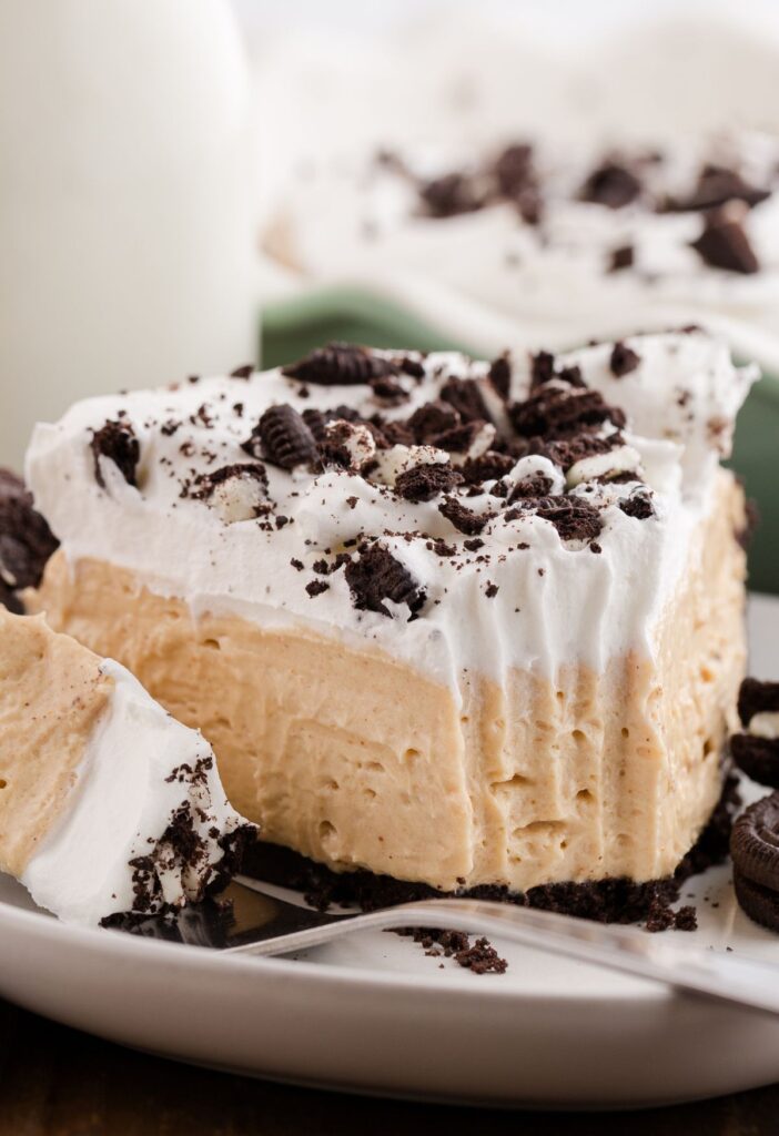 Slice of pie on a white plate with a fork with a bite on it, Oreo crumbs on top of the peanut butter Oreo pie.