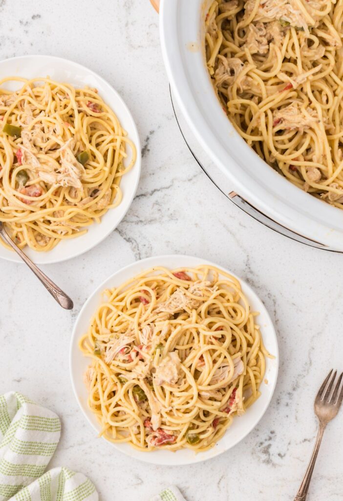 Slow cooker and a serving plate with some chicken spaghetti on it. 