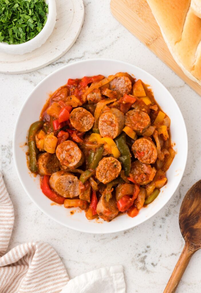 Sliced sausages on a white serving plate with peppers.