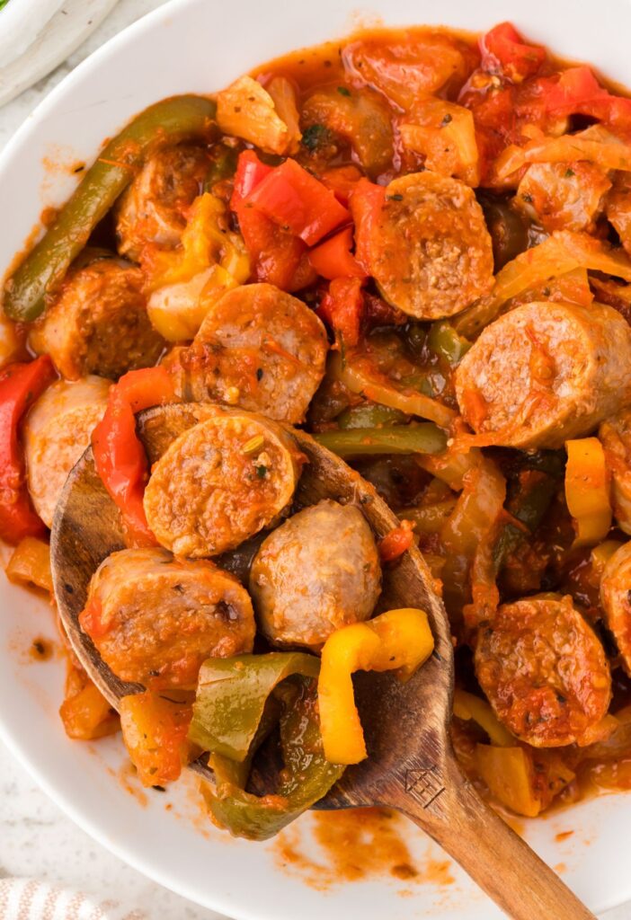 A wooden spoon serving some of the sliced sausages and peppers in marinara sauce. 