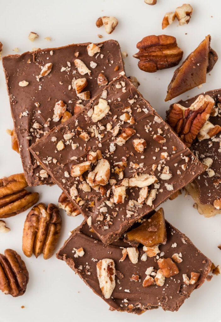 Pile of toffee with pecans on a white plate.