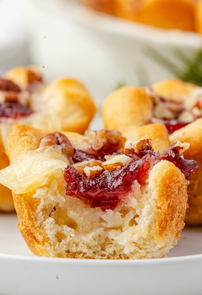 One brie bite on a plate with a bite taken out of it to show the center with brie cheese, cranberry sauce, and pecans.