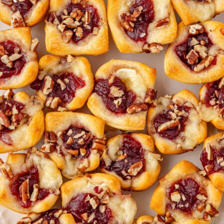Baked brie bites in crescent dough on a serving platter with fresh rosemary sprigs on the side.