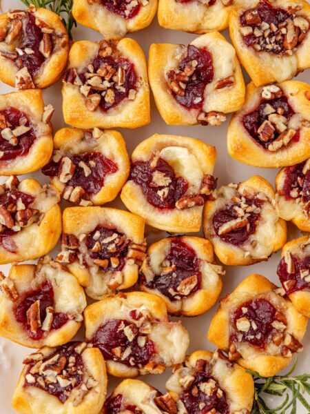 Baked brie bites in crescent dough on a serving platter with fresh rosemary sprigs on the side.