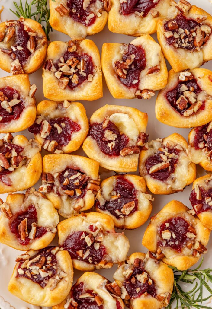 Baked brie bites in crescent dough on a serving platter with fresh rosemary sprigs on the side.