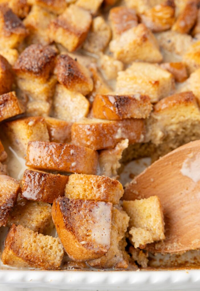 Casserole dish of the eggnog bread pudding with a wooden serving spoon. 